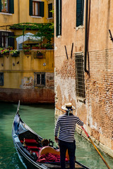 Fototapeta na wymiar Venetian gondolier punting gondola through narrow canal waters of Venice, Veneto, Italy