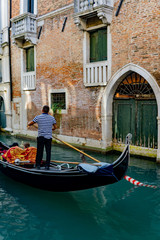 Fototapeta na wymiar Venetian gondolier punting gondola through narrow canal waters of Venice, Veneto, Italy
