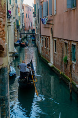 Venetian gondolier punting gondola through narrow canal waters of Venice, Veneto, Italy