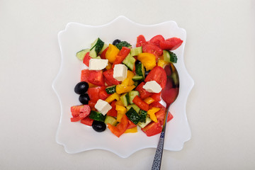 Square plate with fresh greek salad on a light tablecloth.