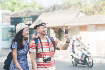 Naklejka premium two young backpackers taking selfies using mobilephones camera