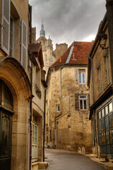Fototapeta na wymiar Narrow street in the beautiful old French town Dole, the steeple of the church of Notre-Dame and dark clouds above the old houses