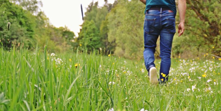 Close-up on the feet - man is walking in the summer through a green meadow