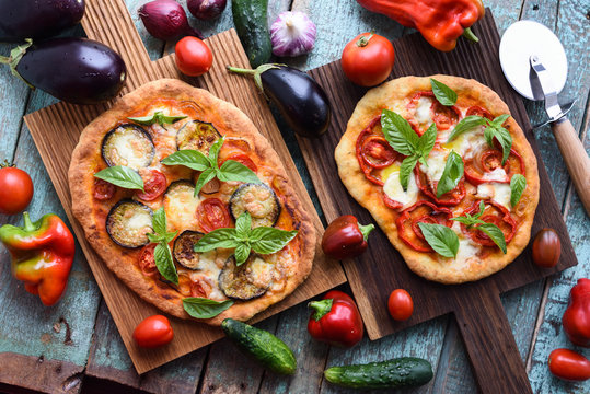 Healthy vegetarian food. Homemade Italian pizzas with aubergines, tomatoes and basil on oak cutting boards with raw vegetables on blue table