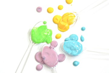 Transparent spoons with different drops of paint on top of a plain background - plastic spoon with color as background background with space for text