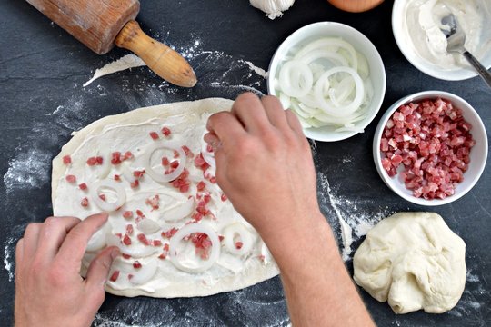 Close-up - Man cook Alsatian tarte cake on a black kitchen surface - next to it are the ingredients for the tarte flamb&eacute;e