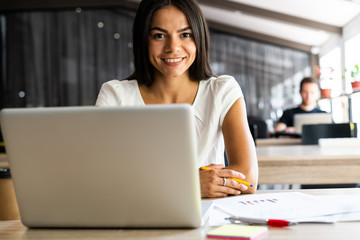 New solution every day. Confident young woman in smart casual wear working on laptop while sitting...