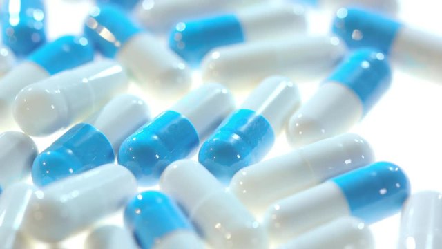 Medicine pills. Close up of white and blue capsules rotating on white table. Pharmaceutical pills on table. Pharmacy industry concept. Medical treatment concept