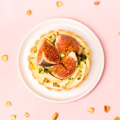 Delicious tart with fresh figs and pistachios on pink pastel backgrounds, top view