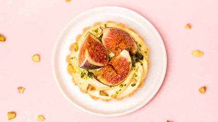 Delicious tart with fresh figs and pistachios on pink pastel backgrounds, top view