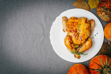 Roasted chicken with thyme served on white plate with potatoes, oranges and spices on gray tablecloth. Thanksgiving or Christmas dinner. Top view