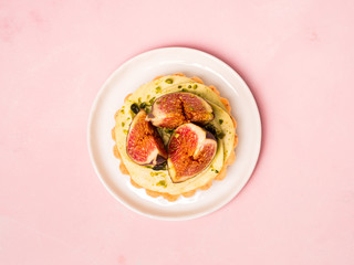 Delicious tart with fresh figs and pistachios on pink pastel backgrounds, top view