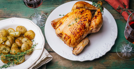 Roasted chicken with thyme served on white plate with potatoes, oranges and spices on wooden table. Thanksgiving or Christmas dinner. Top view