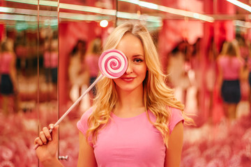 Obraz na płótnie Canvas Young beautiful blonde in a pink blouse on the soft pink background with multi-colored bright pink lollipop