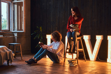 Young student couple reading together in a room decorated with voluminous letters with illumination.