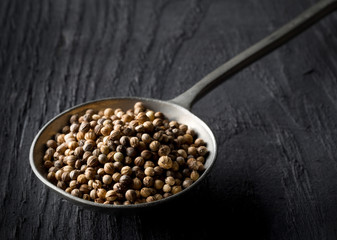 Raw, unprocessed organic coriander or cilantro seeds in metal spoon on wooden table