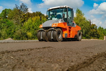 construction machinery for road works passes through new asphalt in the summer on the background of trees