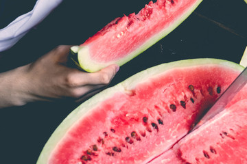 overhead view of male teenager biting a watermelon sitting at the wooden table on summer day d