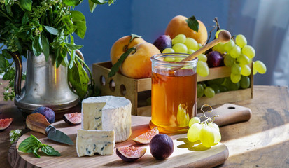 Delicious gourmet cheese Dorblu, honey, with sliced fresh figs and grapes, peaches, on a rustic wooden table
