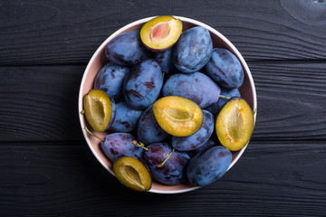 Fresh plums in bowl on wooden table