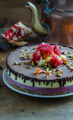 Vegan raw cheesecake with mango, black currant, blueberry, orange,  cashew cream, coconut butter and coconut milk, and base made of almonds, dates  and  dried apricots, oat flakes, lyophilisated berry