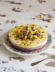 Vegan raw cheesecake with mango, black currant,  cashew cream, coconut butter and coconut milk, and base made of almonds, dates  and  dried apricots, oat flakes, lyophilisated berry