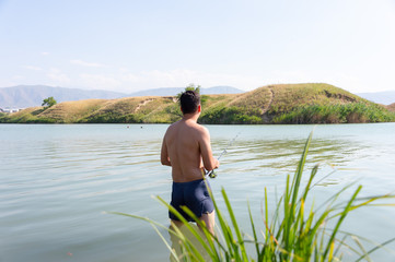 Fisherman with a fishing rod on the river bank. A fisherman is fishing. Fish, rotating coil. - The concept of rural recreation. Article about fishing.