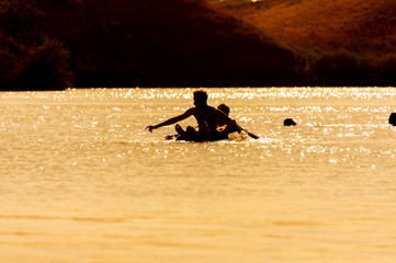 people swim on an inflatable mattress in the water at sunset time