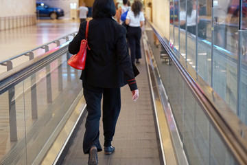 Fototapeta premium Woman at horizontal escalator covered. Moving walkway, moving sidewalk, moving pavement, autopedescalator, walkalator, travelator, autowalk, horizontal escalator, slidewalk, or moveator at an airport.
