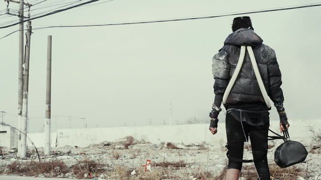 postapocalypse, lonely young woman walks amid garbage dump and abondoned town
