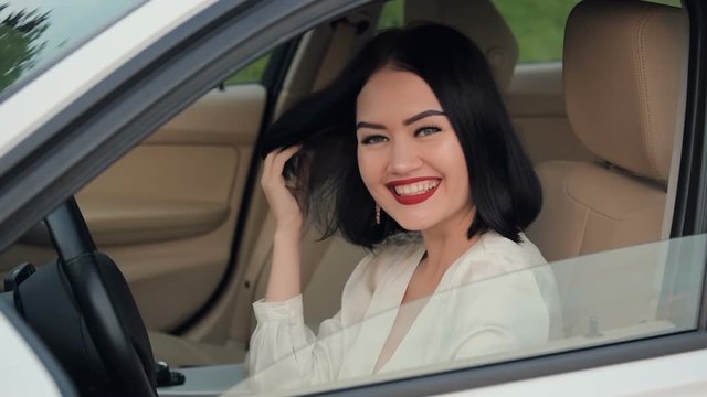 Portrait of pretty, happy woman flirting to camera sitting in car. Talking to another car driver in a traffic jam. Slow motion.
