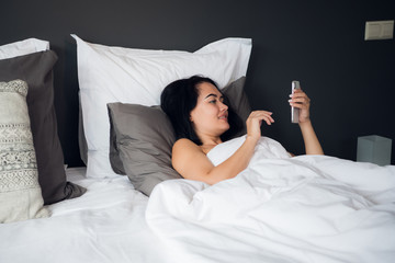 Young female connect social network with smartphone in the morning, she relax on white bed