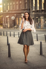 Obraz premium Young fashionable woman dressed in retro clothes using her cell phone, enjoying a beautiful day in the city