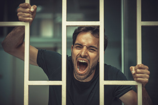 Solitude concept, man behind prison or cage bars trying to break free, mentally ill and deranged