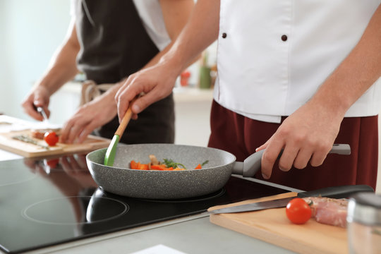 Male chef cooking vegetables on electric stove, closeup
