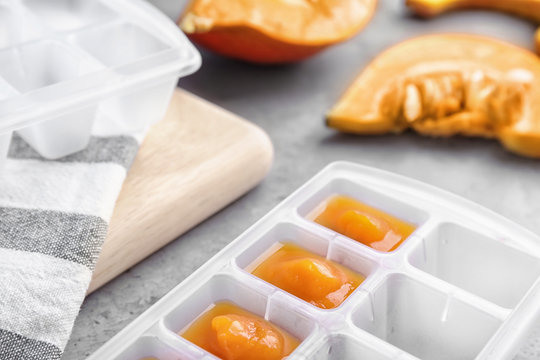 Ice cube tray with healthy baby food on gray table