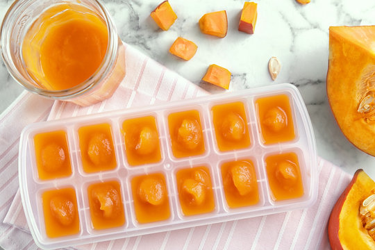 Flat lay composition with ice cube tray of baby food on marble background