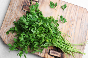 Wooden board with fresh green parsley on light fabric, top view