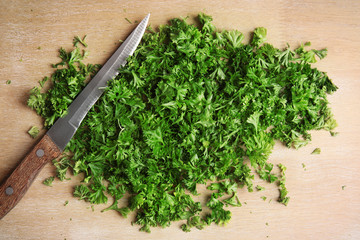 Chopped parsley and knife on wooden background, top view