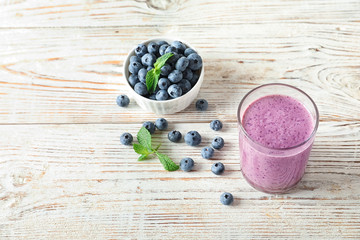 Tasty blueberry smoothie in glass and bowl with fresh berries on wooden table