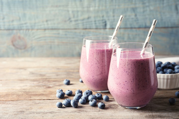 Tasty blueberry smoothie in glasses and berries on wooden table against color background with space...