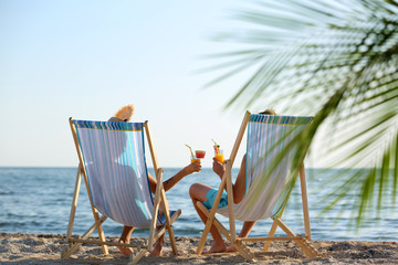 Naklejka premium Young couple with cocktails in beach chairs at seacoast