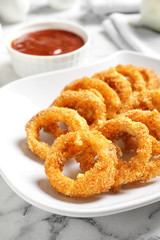 Plate with homemade crunchy fried onion rings and sauce on marble table, closeup