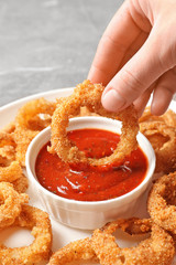 Woman dipping crunchy fried onion ring in tomato sauce, closeup