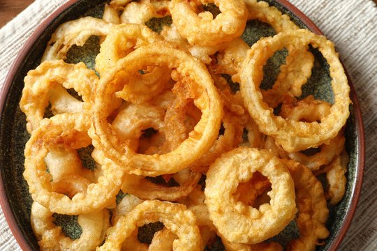 Homemade crunchy fried onion rings on plate, top view