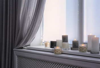 Burning candles on window sill in room