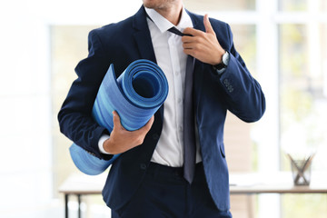 Young handsome businessman holding yoga mat in office. Gym after work