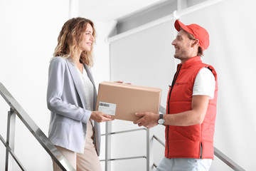 Young woman receiving parcel from courier indoors