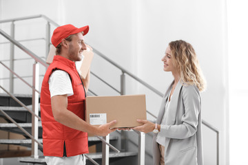 Young woman receiving parcel from courier indoors