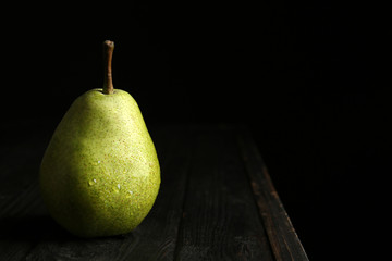 Ripe pear on wooden table against dark background. Space for text